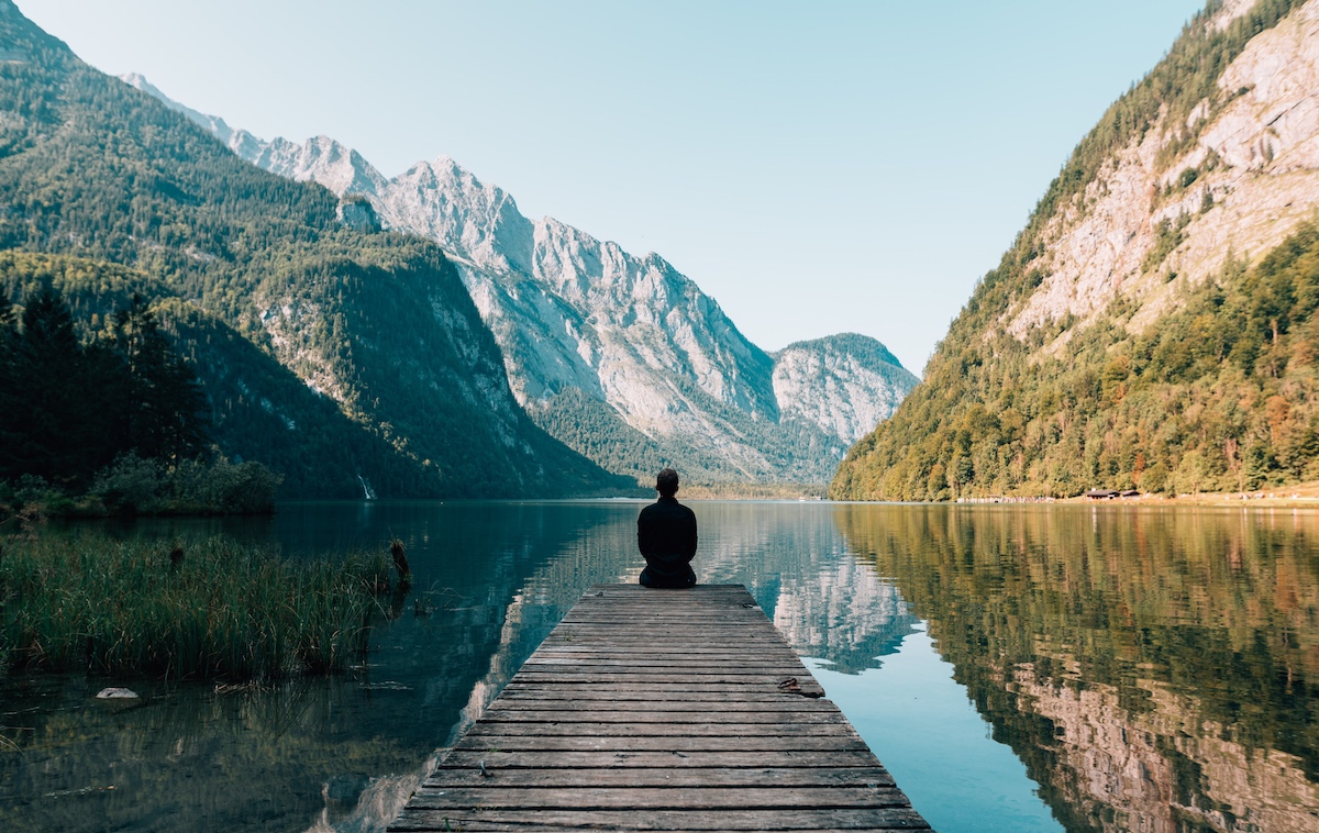 man quietly sitting on a dock with lake and mountains